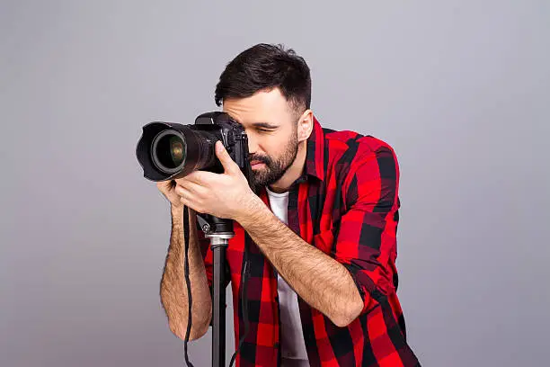 Portrait of male photographer with  professional camera isolated on gray background