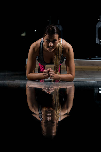 woman in a gym exercising, doing push ups. dark background - human muscle flash imagens e fotografias de stock
