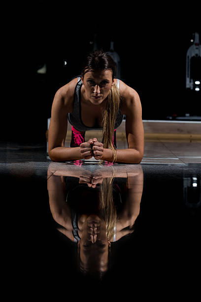 mujer en un gimnasio haciendo ejercicio, haciendo flexiones. fondo oscuro - human muscle flash fotografías e imágenes de stock