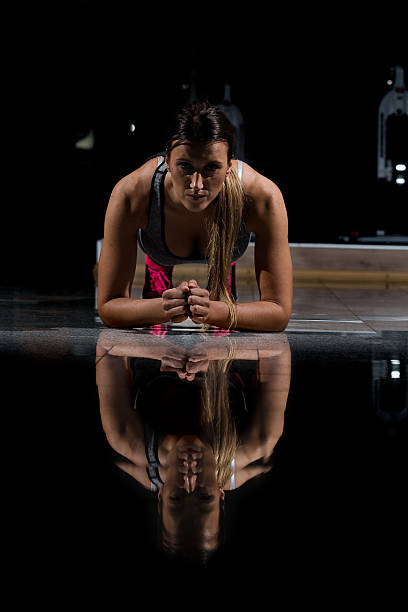 woman in a gym exercising, doing push ups. dark background - human muscle flash imagens e fotografias de stock