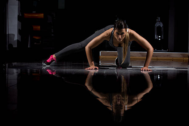 mulher em uma academia se exercitando, fazendo flexões. fundo escuro - human muscle flash - fotografias e filmes do acervo