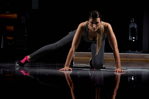 mujer en un gimnasio haciendo ejercicio, haciendo flexiones. fondo oscuro - human muscle flash fotografías e imágenes de stock
