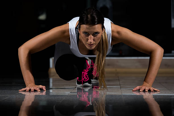 mulher em uma academia se exercitando, fazendo flexões. fundo escuro - human muscle flash - fotografias e filmes do acervo