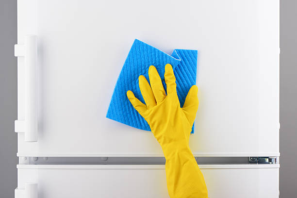 istock Hand in yellow glove cleaning white refrigerator with blue rag 636372266