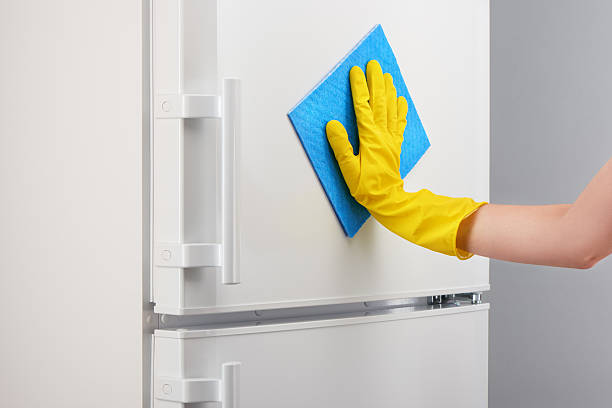 istock Hand in yellow glove cleaning white refrigerator with blue rag 636372298
