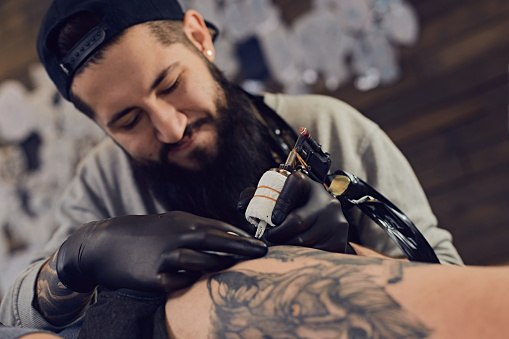 Tattoo master in black gloves, tattoo on the skin of black ink tattoo of his client in the salon.