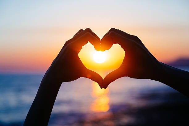 hands forming a heart shape with sunset silhouette - love hand sign stockfoto's en -beelden