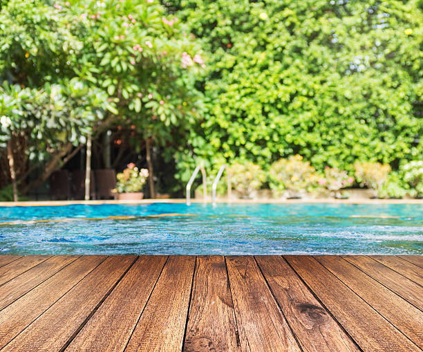 istock Wooden plank floor against swimming pool with green trees 636384048