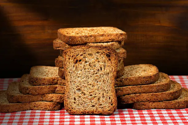 Group of healthy rusks of wholemeal flour on a table with red and white checkered tablecloth and wooden dark wall