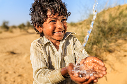 Indian little boy is drinking fresh water, desert village, Thar Desert, Rajasthan, India. Potable water is very precious on the desert - Rajasthani women and children often walk long distances through the desert to bring back jugs of water that they carry on their heads. 