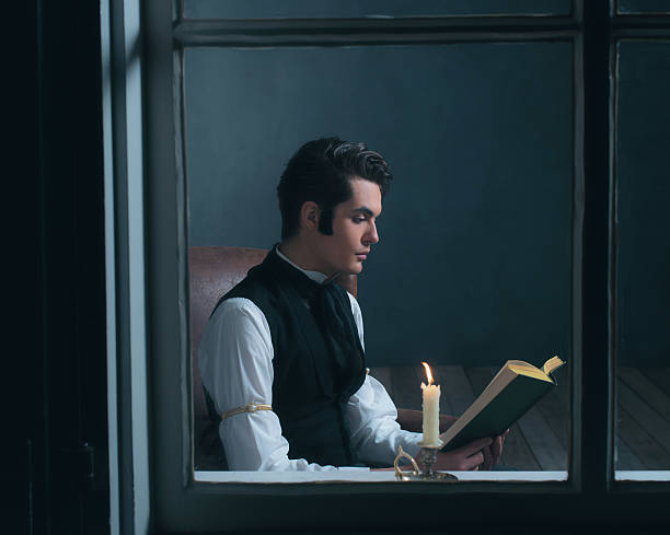 istock Retro victorian man reading book by candlelight sitting by window. 636399986