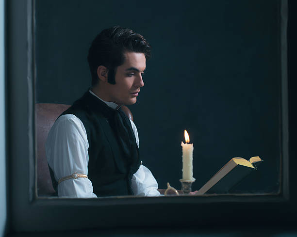 istock Retro victorian man reading book by candlelight sitting by window. 636400038