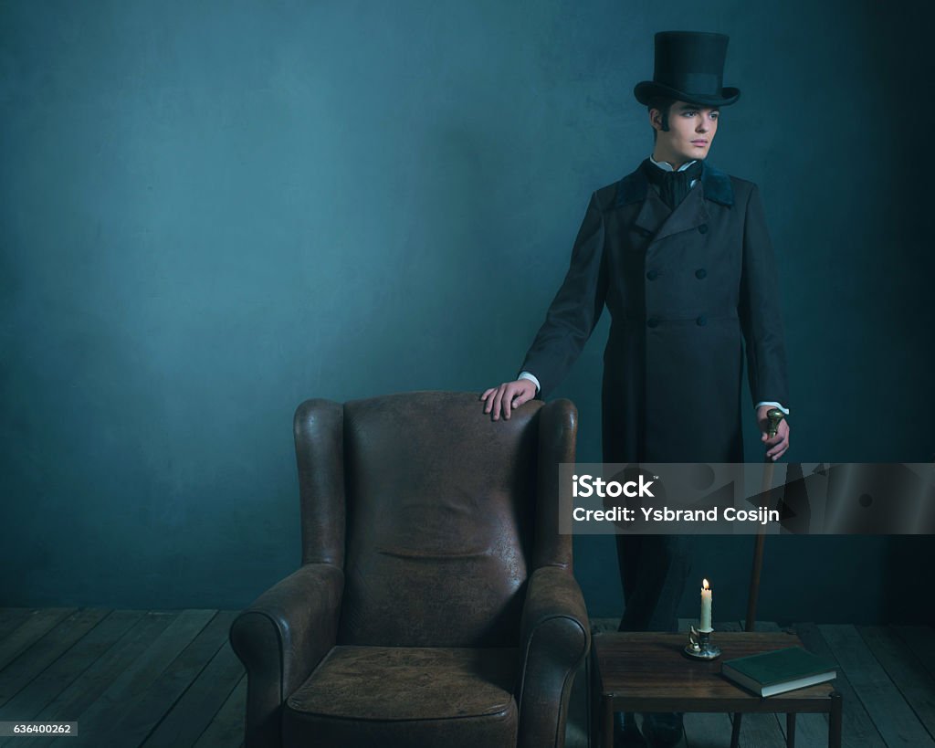 Retro dickens style man standing with cane next to chair. Retro dickens style man standing with cane next to leather chair. Men Stock Photo