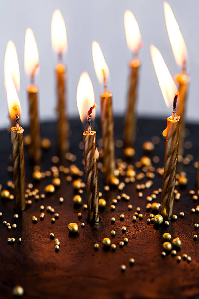 istock Black round birthday cake with burning golden candles 636401254