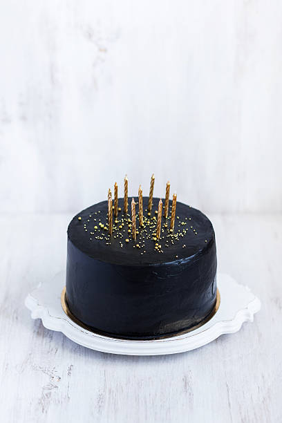 istock Black birthday cake with golden candles on white background 636401428