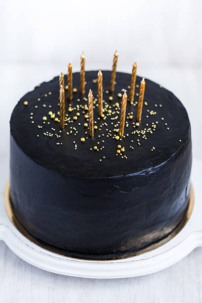 istock Black birthday cake with golden candles on white background 636401474
