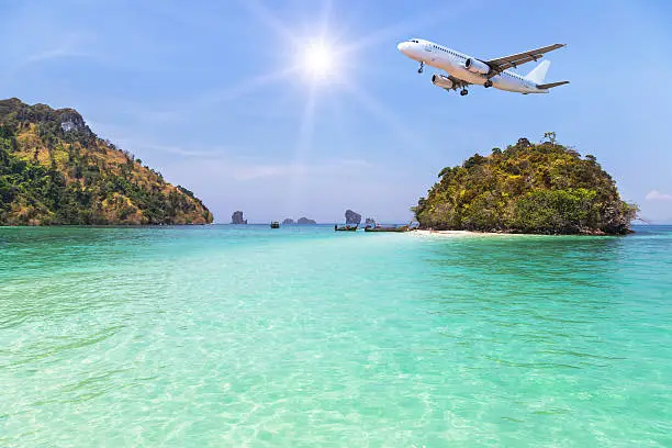 Photo of airplane landing above small island on blue sky with sunlight.