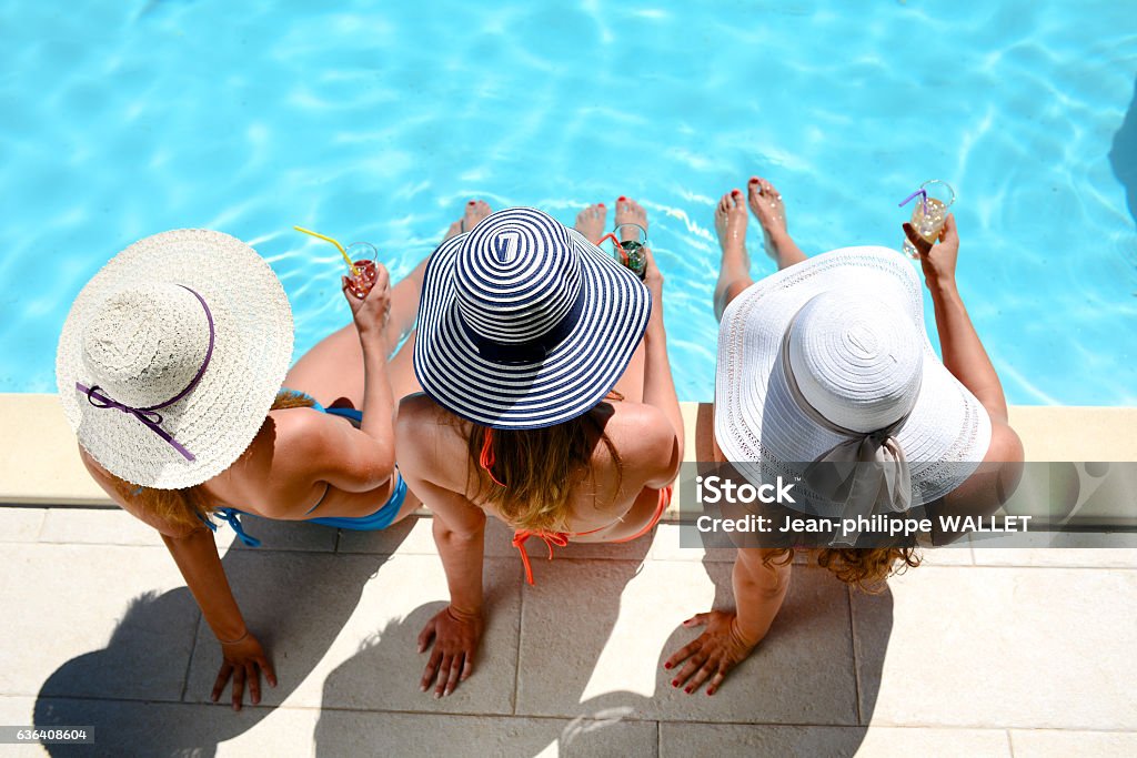 young woman sun hat sitting poolside resort pool summer holiday three beautiful young woman with sun hat sitting by the poolside of a resort swimming pool during summer holiday Swimming Pool Stock Photo