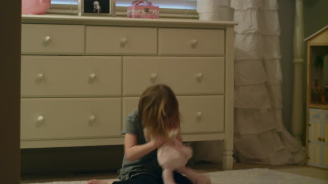 Angry young girl stomps around in her bedroom throwing, hitting and biting a stuffed animal