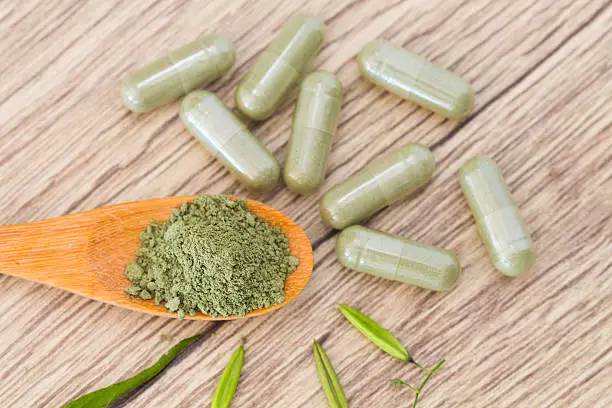 Green herb powder capsules and erlenmeyer flask with green herbal powder capsules ,green herbal capsule on wooden spoon over green background.