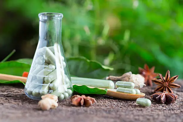 Green herb powder capsules and erlenmeyer flask with green herbal powder capsules ,green herbal capsule on wooden spoon over green background.