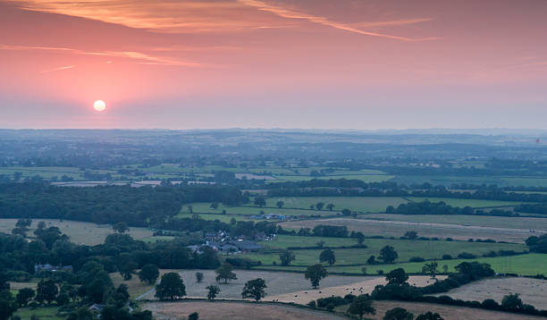 Blackmore Vale sunset The setting sun casts a red sky through dusty haze over the patchwork of dairy pasture, crop fields and woodland that makes up the rural Blackmore Vale farmland district of Dorset, viewed from Bulbarrow Hill in the Dorset Downs. blackmore vale stock pictures, royalty-free photos & images