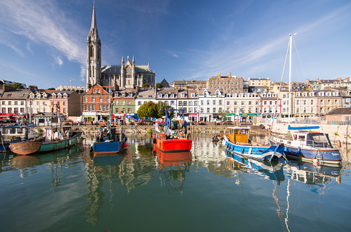 Cork, Ireland - September 15, 2016: The dominating form of St Colman's Cathedral rises above the terraced streets and colourful fishing boats of the small tourist city of Cobh on Cork Harbour.