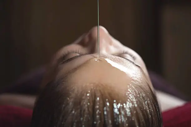 Young caucasian woman enjoying a shirodhara ayurvedic treatment.