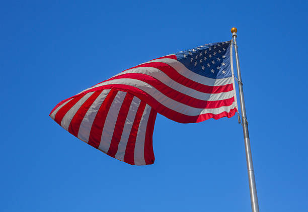 istock American flag flapping on a wind, with blue sky background 636471336