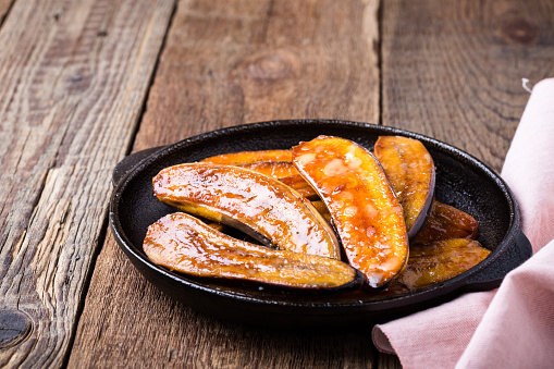 Homemade caramelised banana in  cast iron frying pan on wooden rustic pan, vegan dessert