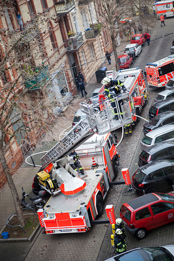 Wiesbaden, Germany - December 8, 2016: Fire vehicles, ambulances and rescue workers at the place of action of a house fire in the city center of Wiesbaden. In the foreground a firefighter on a fire ladder. High-angle view.