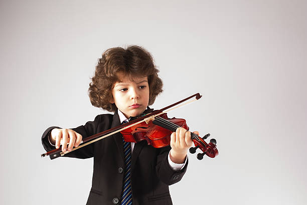 istock Little curly boy thoughtfully, playing a musical instrument. Gray background. 636477338
