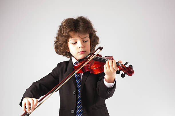 Little curly boy playing a musical instrument. Gray background.