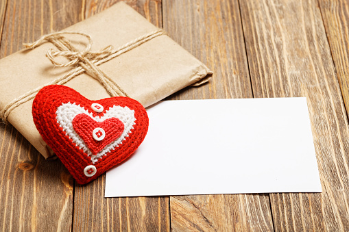 Mockup Valentines day greetings. Gift parcel, white blank label for greeting text and small handmade red heart on wooden background.