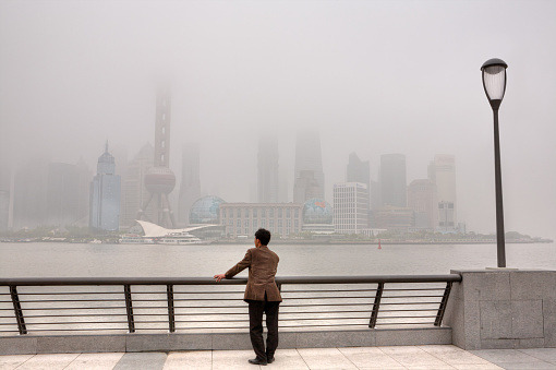Shanghai, China - April 20, 2010: Air Pollution, high-rises shrouded in heavy smog,  air in City remained severely polluted, man standing on the Bund, and looks at the Pudong District.