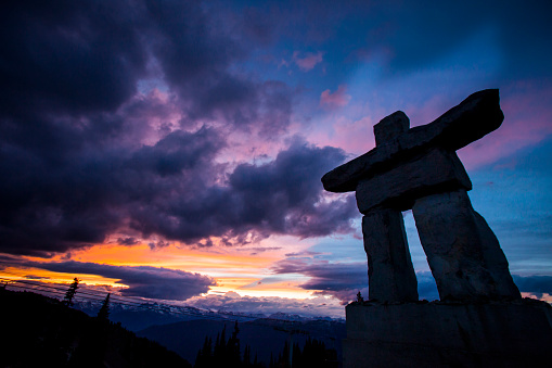 Silhouette of inukshuk with dramatic sunset sky in background.