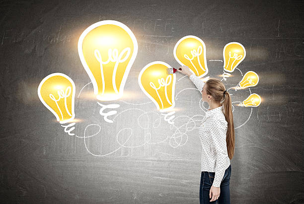 istock Woman with long blond ponytail drawing yellow light bulbs 636489214