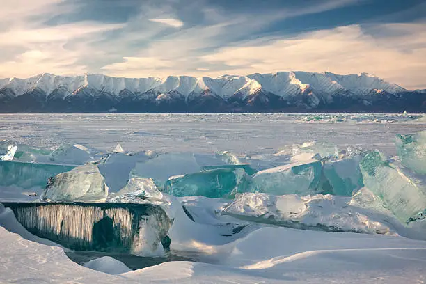 Lake Baikal in winter. Ice hummlocks and icicles on foreground. Mountains of Svyatoy Nos peninsula on background