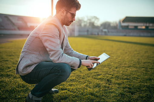 Young and successful footbal manager holding a digital tablet out on the football field.