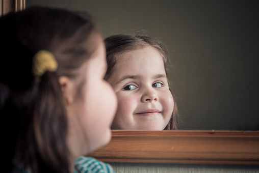 Sweet and comely little girl in front of a mirror, smiles.