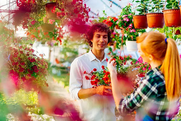 Cheerful young couple choosing potted flowers in plant nursery for home decoration. Young red head woman and handsome young man in casual clothing buing flowers. Image taken with Nikon D800 and 50mm lens, developed from RAW.