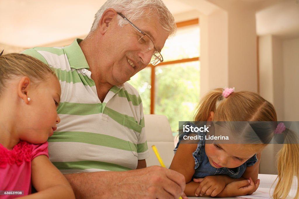 Grandfather working homework with granddaughters. Private class. Senior man working homework with two little girls. Adult Stock Photo