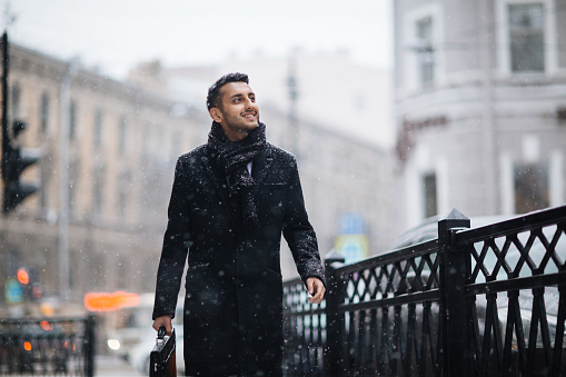 Businessman in coat enjoying winter day while walking in snowfall