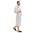 Young man in a bathrobe holding a cup and walking