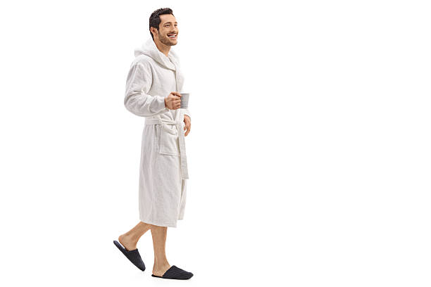 Young man in a bathrobe holding a cup and walking Full length portrait of a young man in a bathrobe holding a cup and walking isolated on white background bathrobe photos stock pictures, royalty-free photos & images