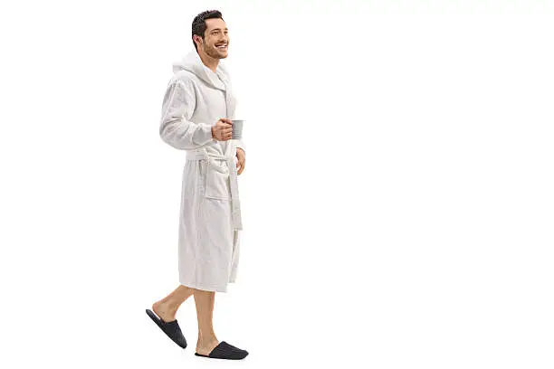 Photo of Young man in a bathrobe holding a cup and walking