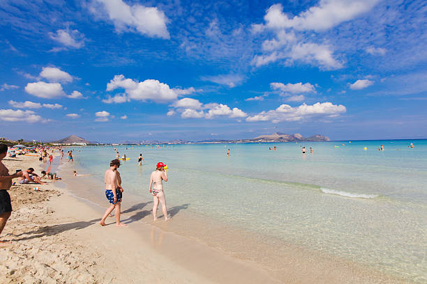 Alcudia, Mallorca - October 2, 2016: The famous beach of Alcudia on Mallorca, Spain. Lots of tourists are walking in the shallow water to cool down from the heat. The beach is famous for its turquoise water.