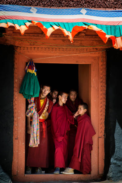 Young buddhist monks standing in a door and watching festival Phyang, India - July 15, 2015:  A group of young buddhist monks are standing in a door and are watching the monastery festival in the courtyard of Phyang Monastery, Ladakh. They are dressed in traditional red robes. phyang monastery stock pictures, royalty-free photos & images