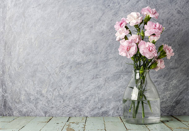 istock Pink carnation flowers in clear bottle on old wood 636563070