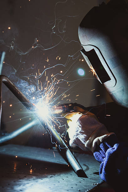 istock Worker with protective mask welding metal, producing sparks and smoke 636572938